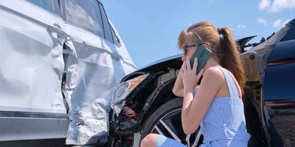 female driver next to wrecked car on the phone