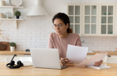 thoughtful hispanic female at home on her laptop and holding papers
