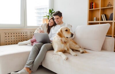 young happy couple on the couch with laptop and dog