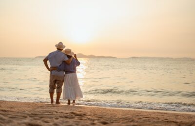 retired couple arm in arm on the beach watching the sunset