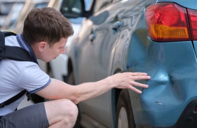 male sitting on street in shock over dent in car