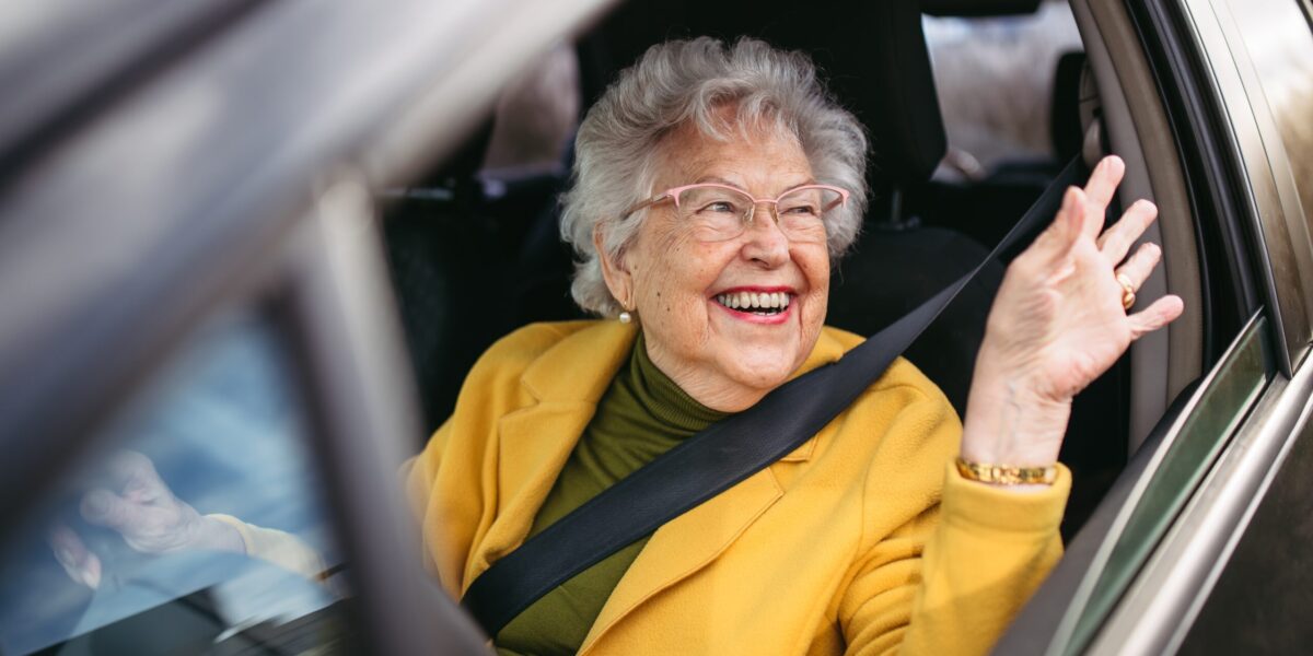happy elderly woman waving and driving a car
