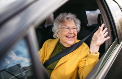 happy elderly woman waving and driving a car