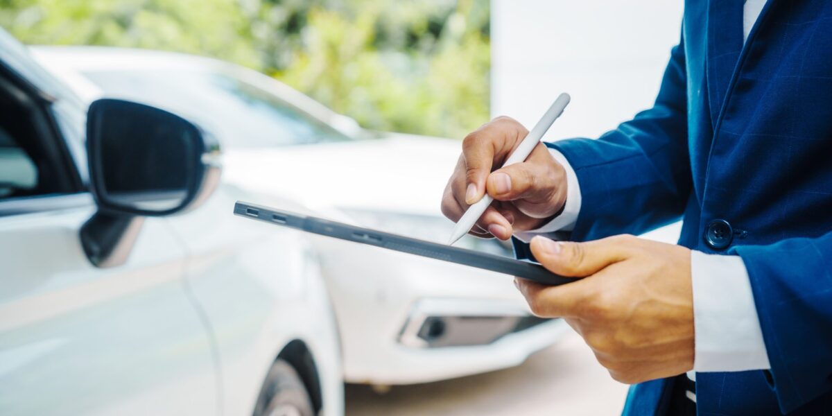 business man taking notes on clipboard next to car